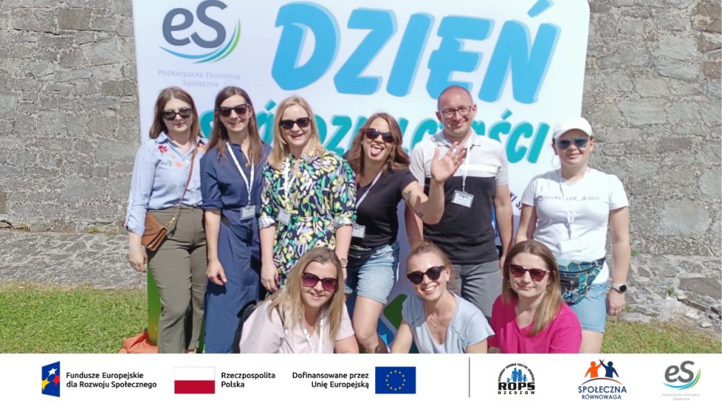 Grupa ludzi pozujących na tle plakatu dnia spółdzielczości