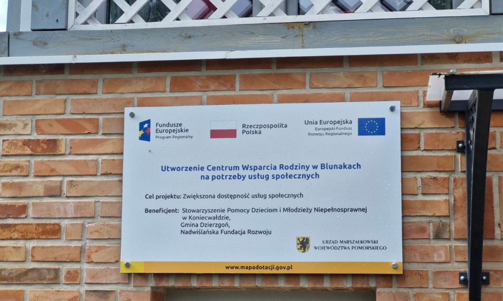 Zdjęcie tabliczki na budynku z tekstem "Utworzenie Centrum Wsparcia Rodziny w Blunakach na potrzeby usług społecznych"