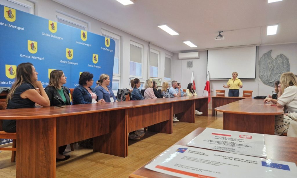 Grupa ludzi siedzących przy biurkach słuchających prelegenta