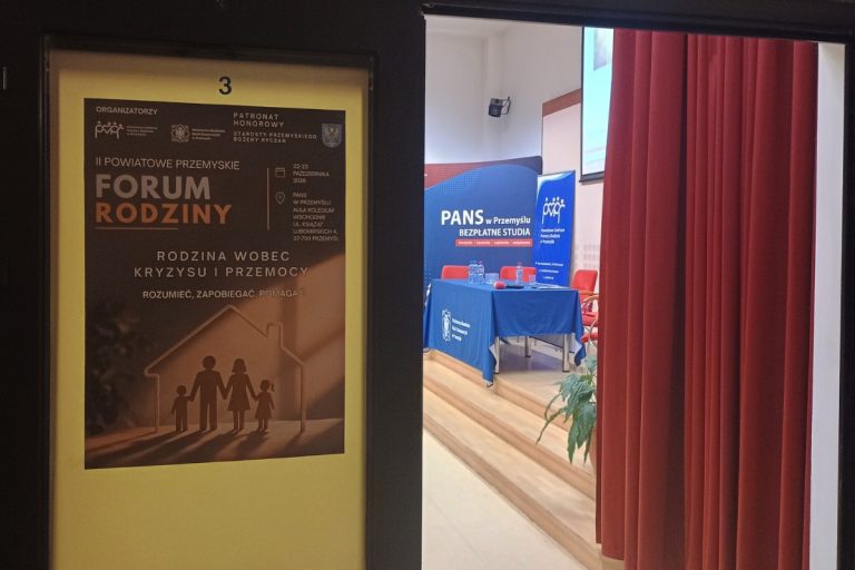 zdjęcie przedstawiające otwarte drzwi do sali z plakatem informującym o wydarzeniu i banerami w tle